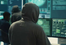 Person in hoodie working at computer monitors.