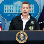 Man speaking at podium with presidential seal and flags