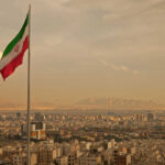 Iranian flag waving over a city skyline with mountains in the background