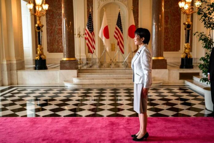 A woman in formal attire standing in a grand hall with flags in the background