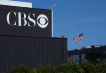 CBS sign on building, American flag in background.
