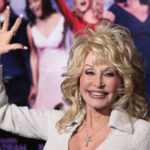 A smiling woman in a glamorous outfit waving at an event