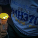 Person holding a lit candle at a memorial for MH370