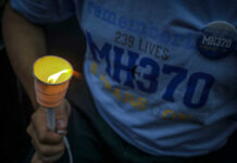 Person holding a lit candle at a memorial for MH370