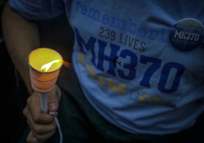Person holding a lit candle at a memorial for MH370
