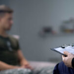A therapist taking notes during a session with a patient in the background