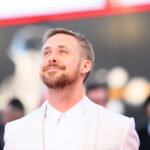 A man in a white suit smiling on the red carpet