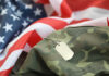 Military dog tags resting on camouflage fabric with an American flag in the background