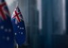 Australian flag displayed on a flagpole with a blurred city background