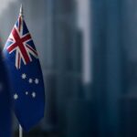 Australian flag displayed on a flagpole with a blurred city background