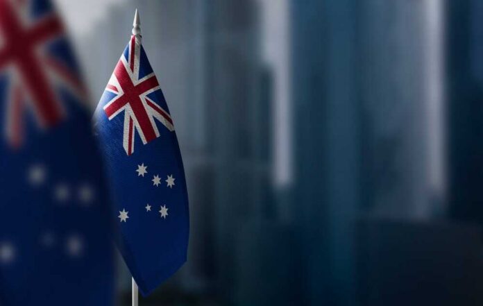 Australian flag displayed on a flagpole with a blurred city background