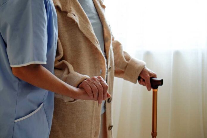 A caregiver holding hands with an elderly person using a cane
