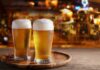 Two glasses of beer on a wooden tray in a bar setting
