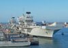Three naval ships docked at a harbor under a clear blue sky