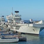 Three naval ships docked at a harbor under a clear blue sky