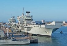 Three naval ships docked at a harbor under a clear blue sky