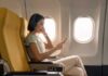 A woman sitting in an airplane seat, wearing headphones and using her phone