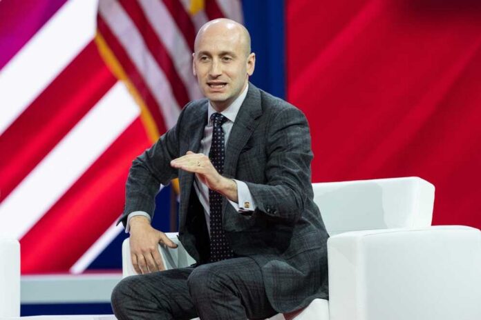 A man in a suit speaking at a conference with an American flag in the background