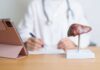 A healthcare professional writing notes with a liver anatomy model and a tablet in view