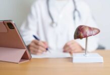 A healthcare professional writing notes with a liver anatomy model and a tablet in view