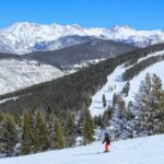 A skier navigating down a snowy slope with mountains in the background