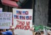 A protester holding a sign that reads 'NO KINGS THIS IS AMERICA' with American flags