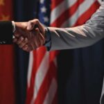 Two individuals shaking hands in front of flags