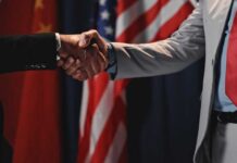 Two individuals shaking hands in front of flags