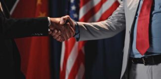Two individuals shaking hands in front of flags