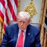 Donald Trump seated in the Oval Office with a serious expression