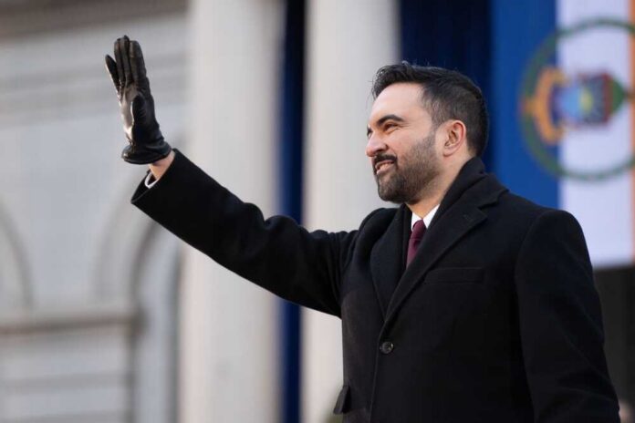 A man in a black coat and gloves waving during a formal event