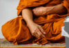 A close-up of a Buddhist monk's hand resting on orange robes during meditation