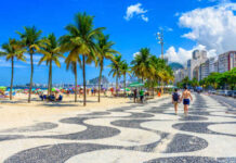 A coastal walkway lined with palm trees and beachgoers enjoying a sunny day