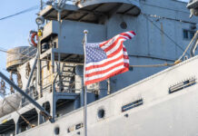 American flag waving in front of a naval ship
