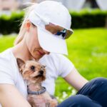 A woman sitting on the grass holding a small dog