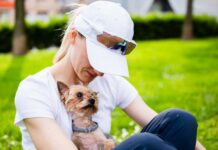 A woman sitting on the grass holding a small dog
