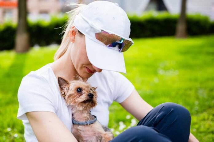 A woman sitting on the grass holding a small dog