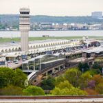 Aerial view of an airport terminal with a control tower and surrounding greenery