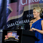 A woman in a blue dress speaking at a charity event podium