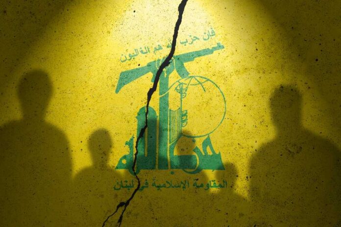Silhouettes of individuals against a yellow wall featuring Hezbollah's emblem