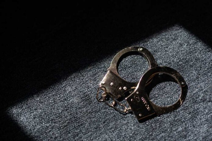 A pair of handcuffs resting on a dark surface with light casting a shadow
