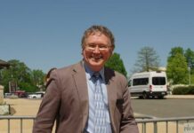 A smiling man in a suit standing outdoors on a sunny day