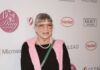 Woman in a pink sweater and glasses smiling at a red carpet event