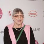 Woman in a pink sweater and glasses smiling at a red carpet event