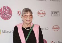 Woman in a pink sweater and glasses smiling at a red carpet event