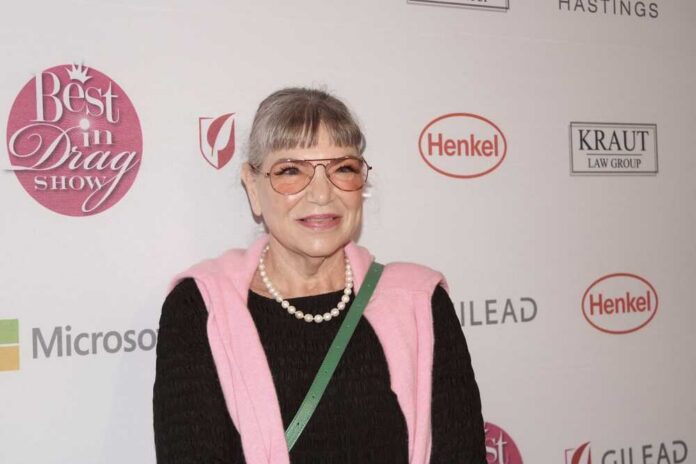Woman in a pink sweater and glasses smiling at a red carpet event
