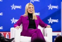 A woman in a bright pink suit smiling while seated on a stage