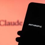 A hand holding a smartphone displaying the word 'ANTHROPIC' against a blurred background