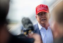A political figure wearing a red cap speaking to the media