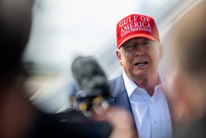 A political figure wearing a red cap speaking to the media